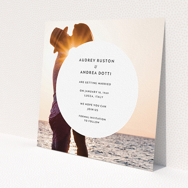 A wedding save the date card design called 'Surrounded'. It is a square (148mm x 148mm) card in a square orientation. It is a photographic wedding save the date card with room for 1 photo. 'Surrounded' is available as a flat card, with mainly white colouring.