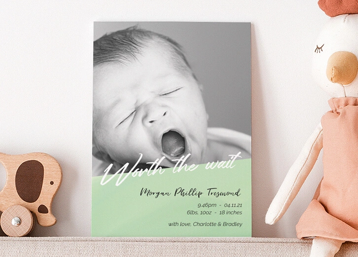 A modern birth announcement card with a baby yawning, styled with wooden toys and pastel decor.