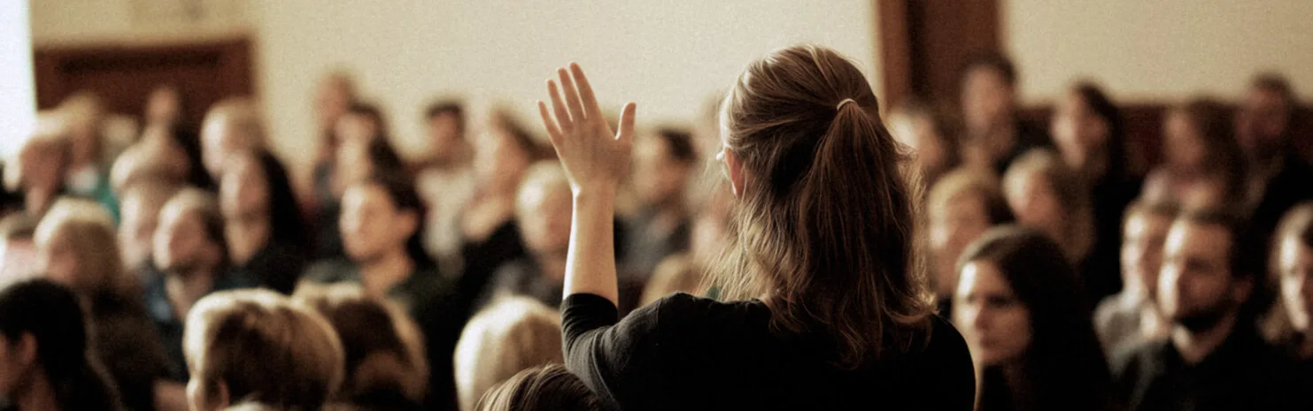 Back view of a woman raising her hand in an audience during a seminar or discussion in a well-lit hall