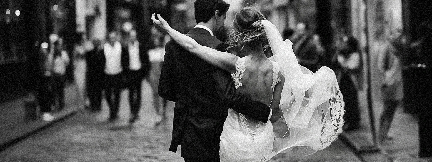 Black and white photo of a bride and groom walking through a street, embracing romantically