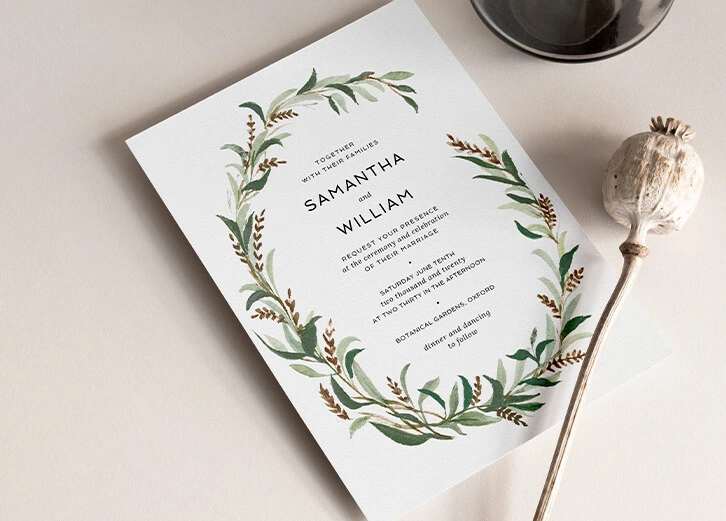 Wedding invitation featuring a natural botanical wreath design in soft green hues.