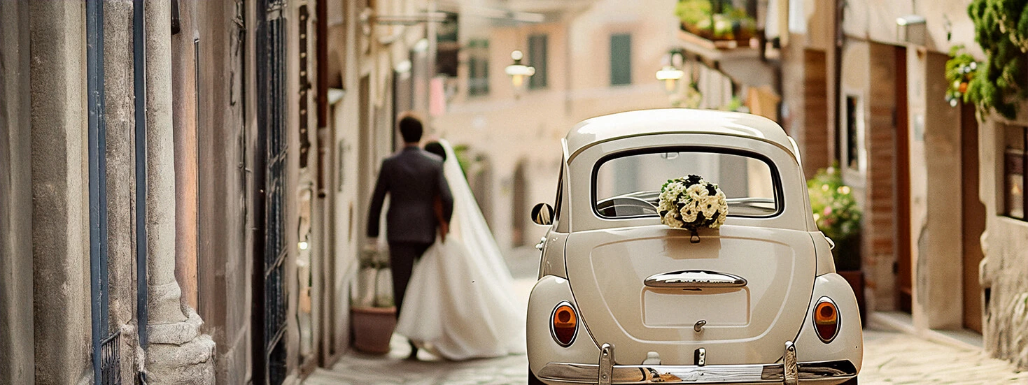 Vintage wedding car decorated with flowers, with a bride and groom walking away in a quaint street