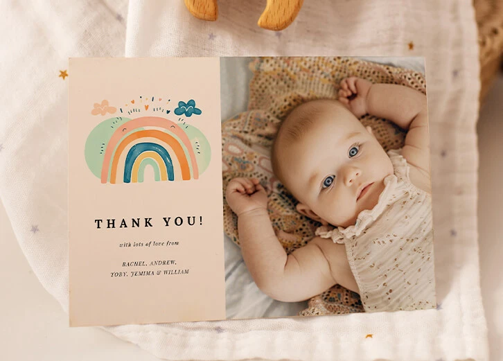 Coordinated birth announcement cards with a rainbow-themed design and a baby photo on a soft fabric background.