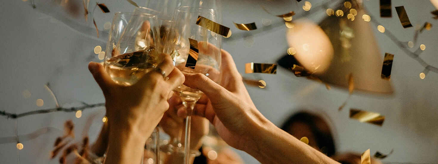 Hands raising glasses in a celebratory toast, with golden confetti falling and warm lights creating a joyful and festive atmosphere.