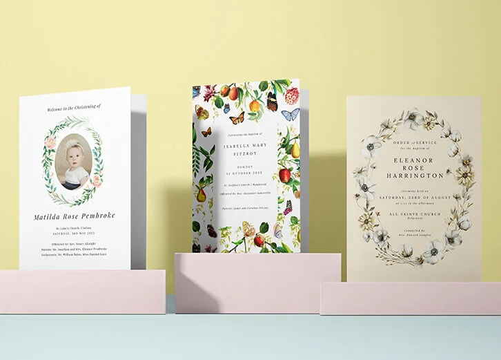 A collection of christening invitations with floral and fruit-inspired themes, displayed on soft pastel blocks.