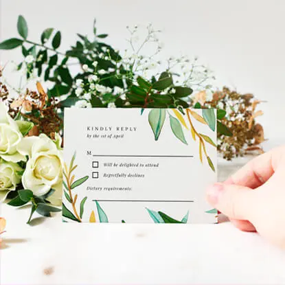 Floral wedding RSVP card with a hand holding it over a flower arrangement