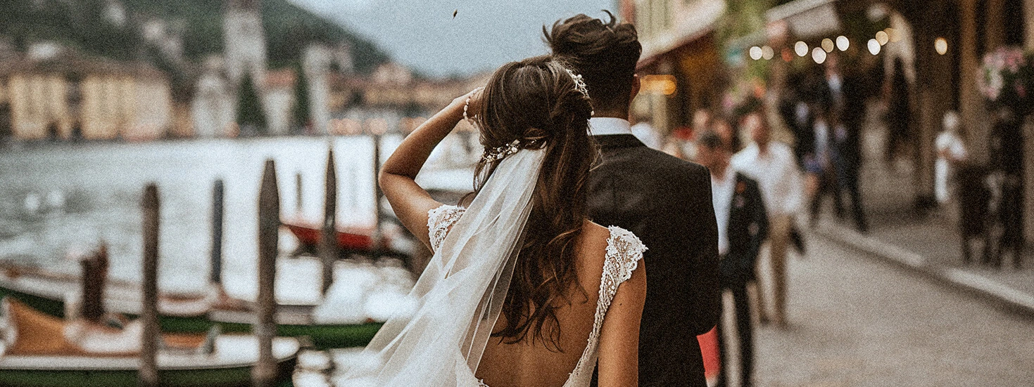 Bride and groom walking along a picturesque lakeside promenade.