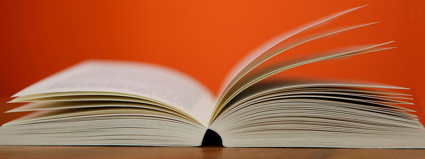 Open book with pages flipping against a vibrant orange background