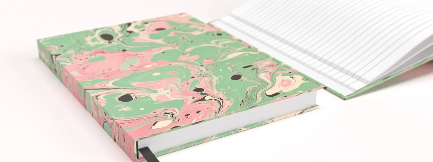 A hardback notebook with a marbled pink and green cover, shown alongside lined pages, designed for personalisation and everyday writing.