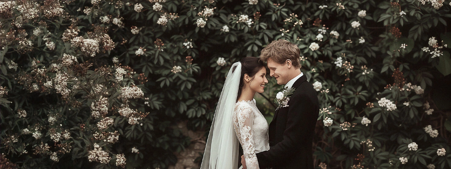 Smiling bride and groom in front of blooming floral backdrop, celebrating their wedding.