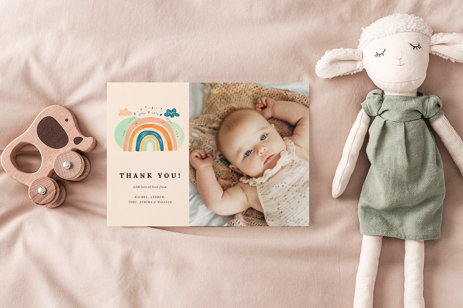 Baby thank you cards featuring a colourful rainbow illustration and a baby photo, displayed on a soft beige fabric