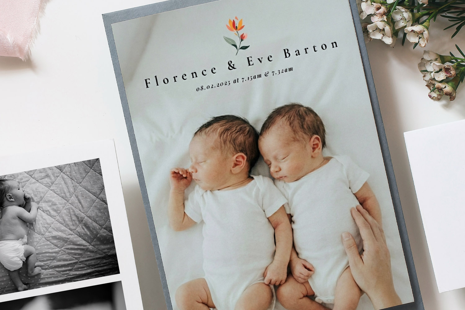 Birth announcement card featuring twin newborns in white sleepsuits, lying side by side with floral detail and names above.