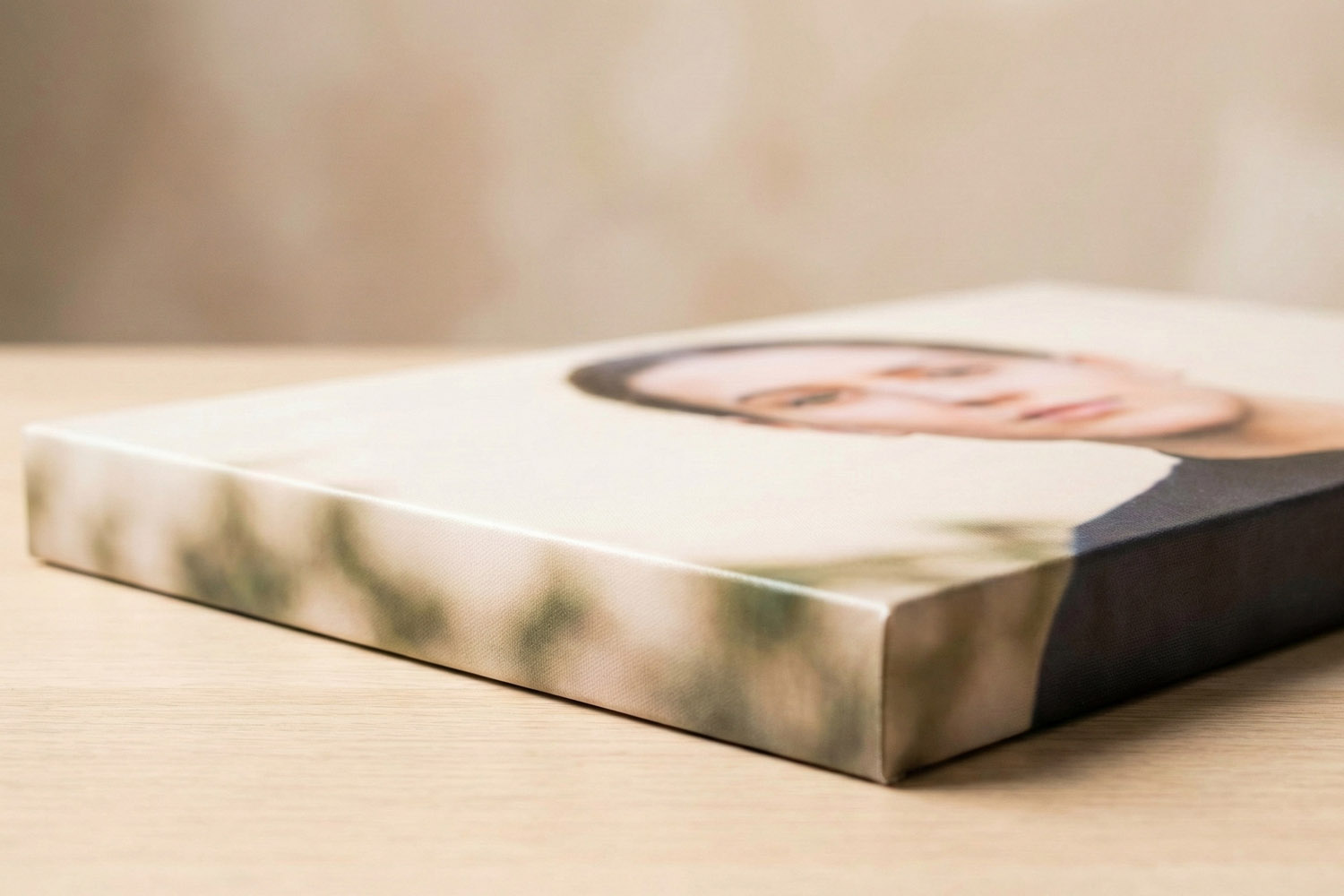 Canvas prints with gallery wrap edges showing a blurred portrait, displayed on a light wooden surface in close-up view.