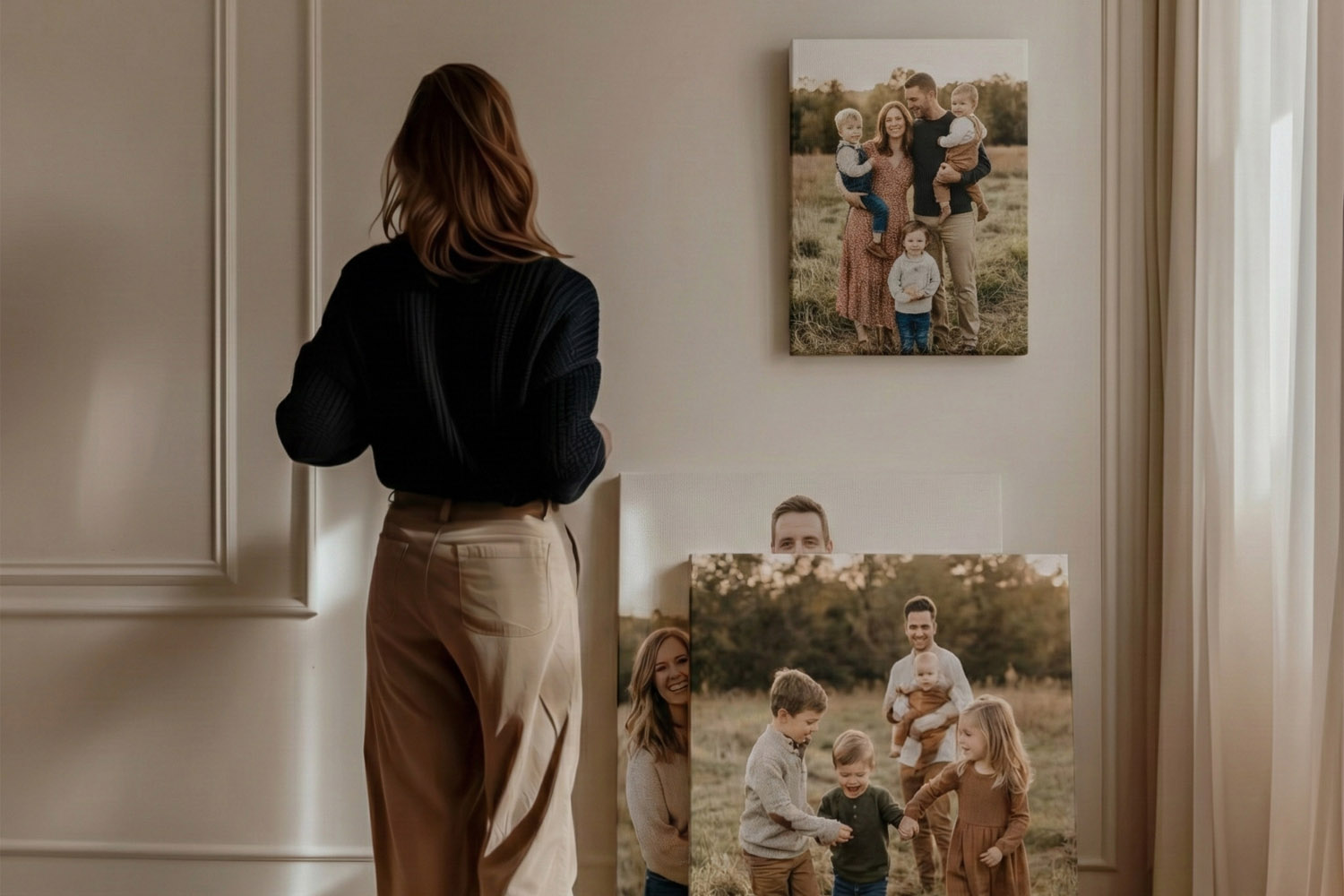 Canvas prints featuring family portraits in warm tones displayed on a cream wall, with a woman viewing the artwork.