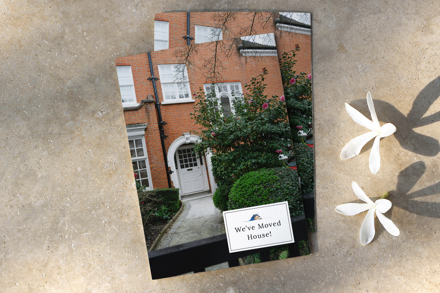 Change of Address Cards featuring a red brick house with a white door and garden, displayed on a stone surface with white