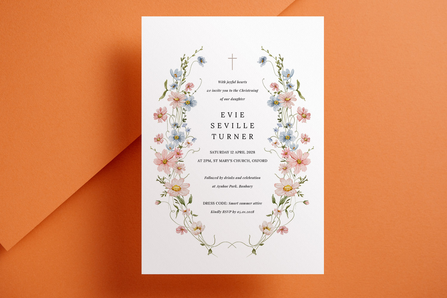 Christening invitations with delicate pastel floral border and elegant typography on white card, displayed on an orange