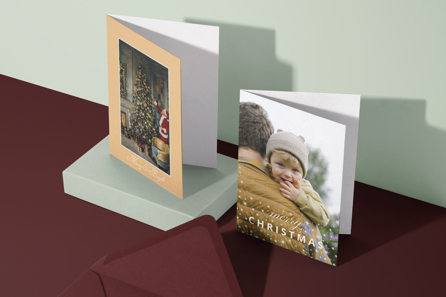 Christmas cards featuring a traditional tree scene and a personalised photo design, displayed upright on a burgundy and