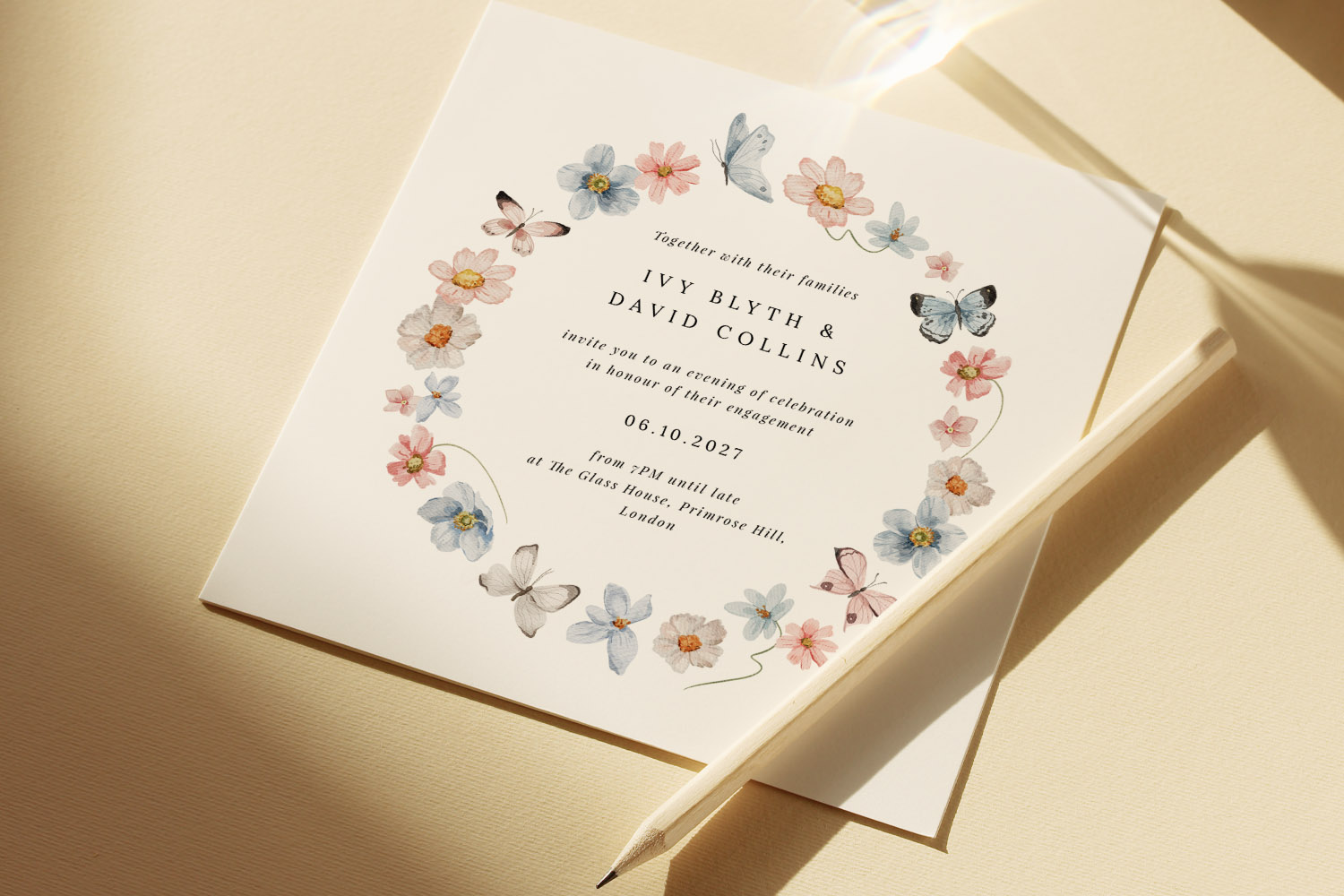 Engagement party invitations with pastel floral and butterfly wreath design on smooth cream card, shown with matching