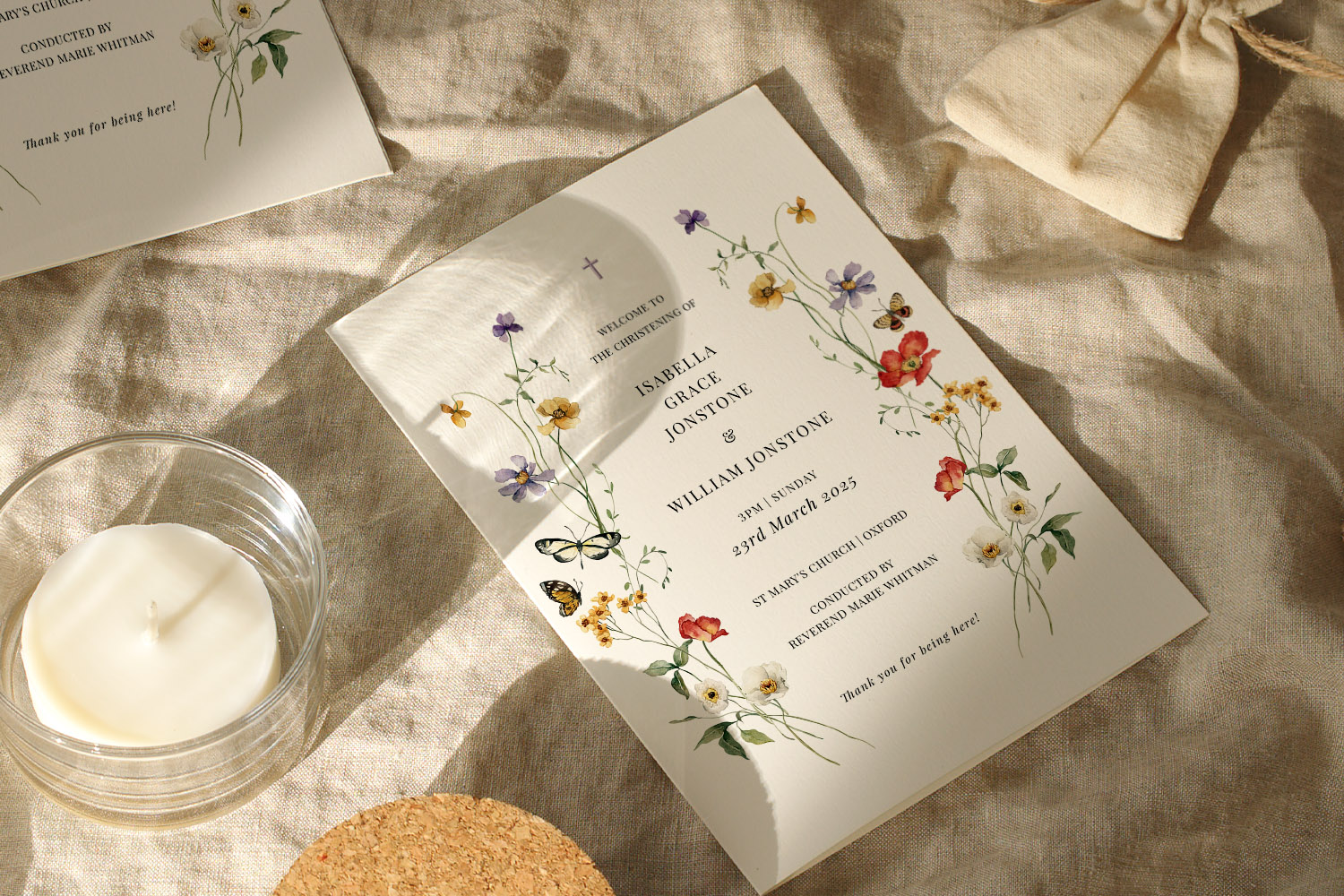 Engagement party invitations with delicate wildflower illustrations on cream card, styled on linen with a candle and pouch