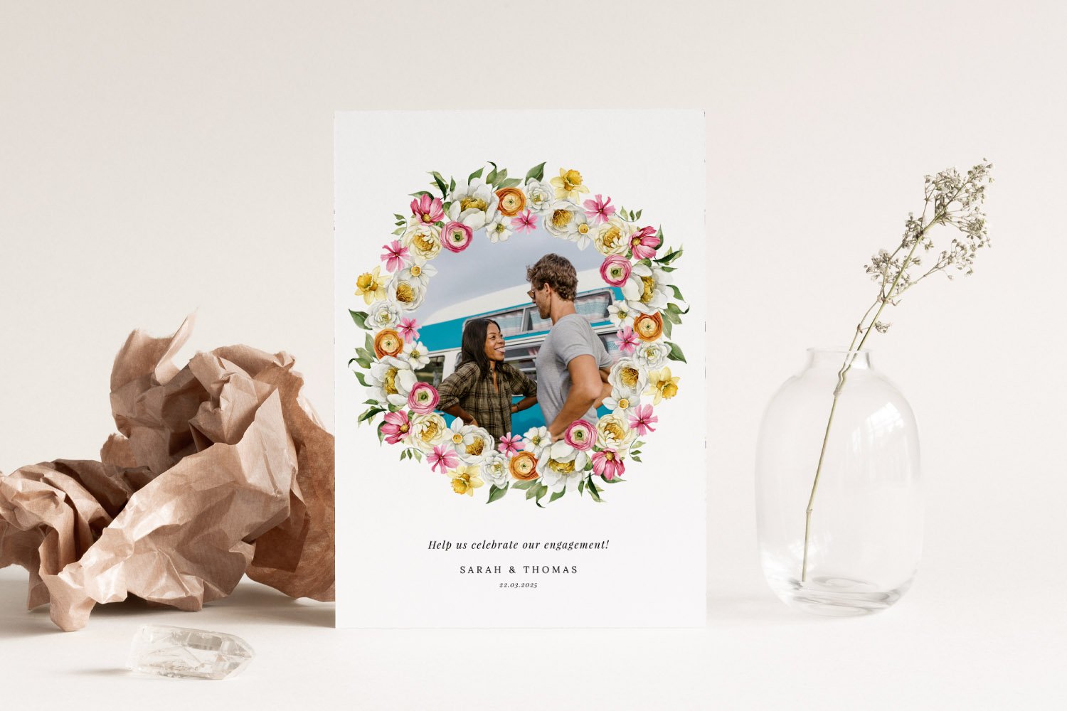 Engagement party invitations with a floral wreath design and a couple's photo, displayed upright on a neutral background.