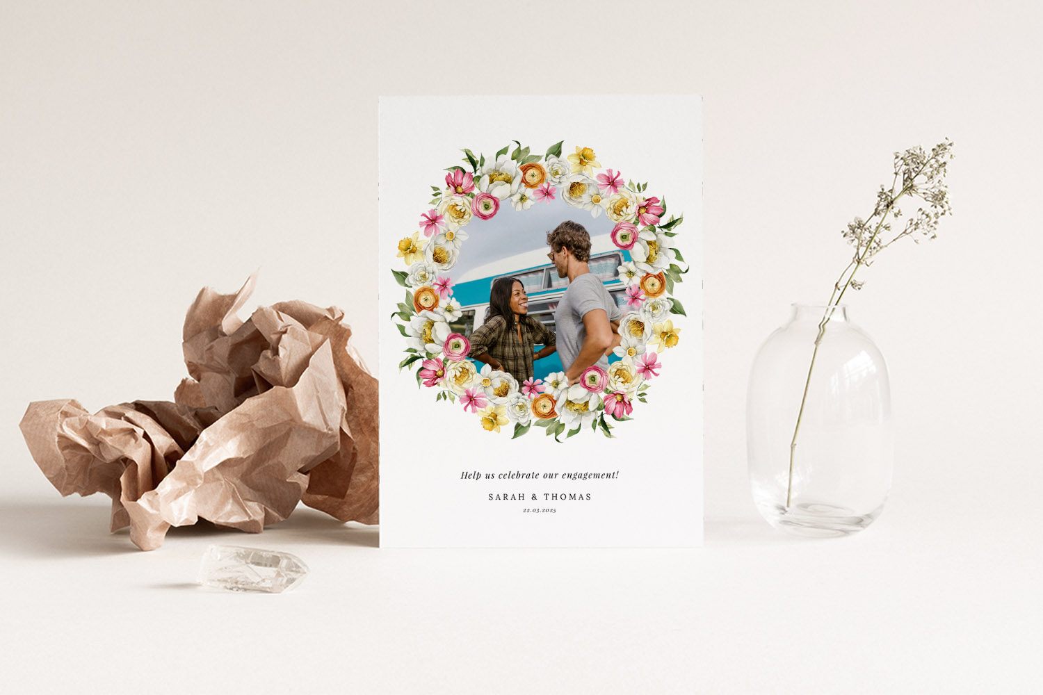 Engagement party invitations featuring a floral wreath design with a couple's photo, displayed upright on a neutral