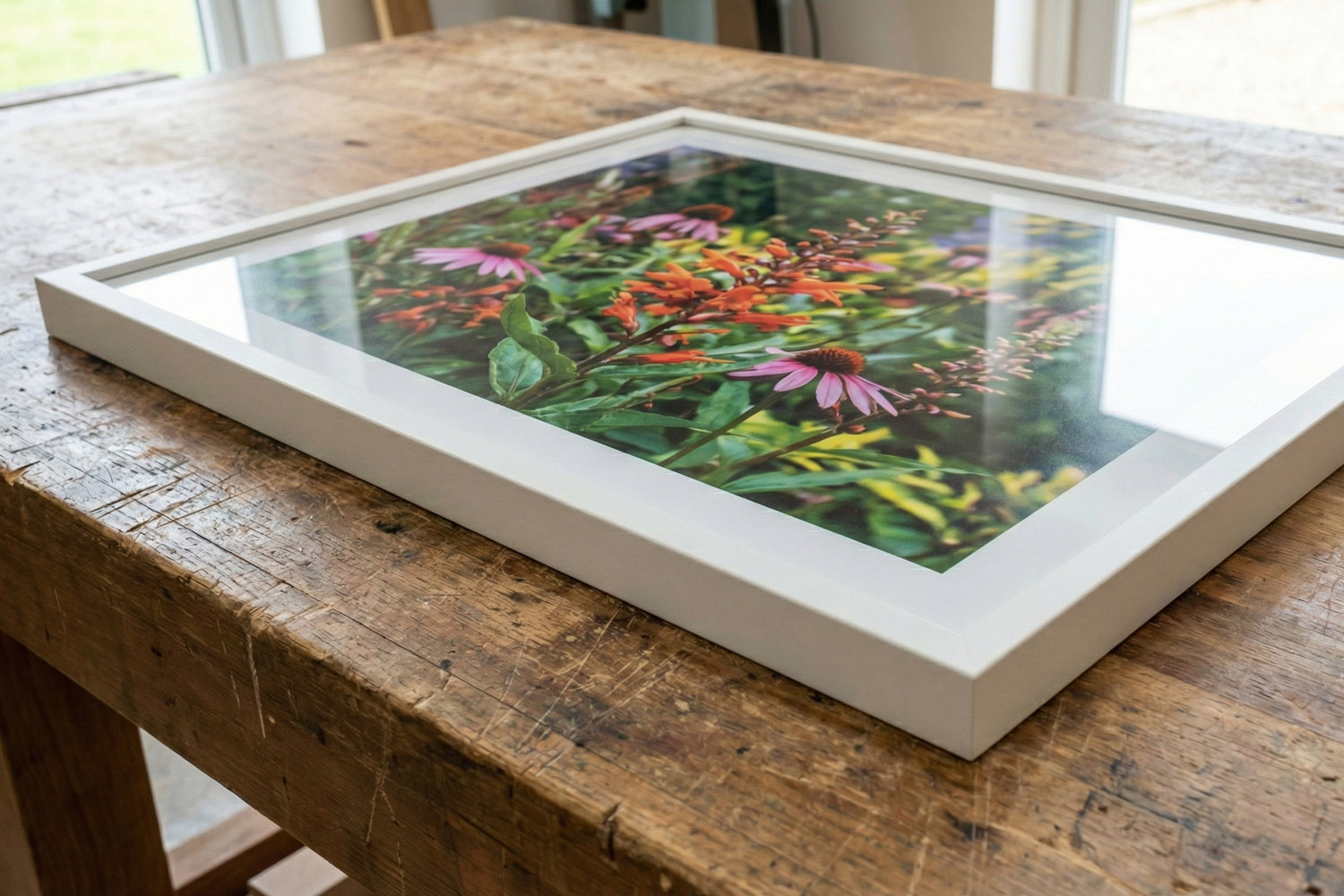 Framed and mounted prints featuring a colourful floral artwork in a white frame with clear glazing on a rustic wooden table