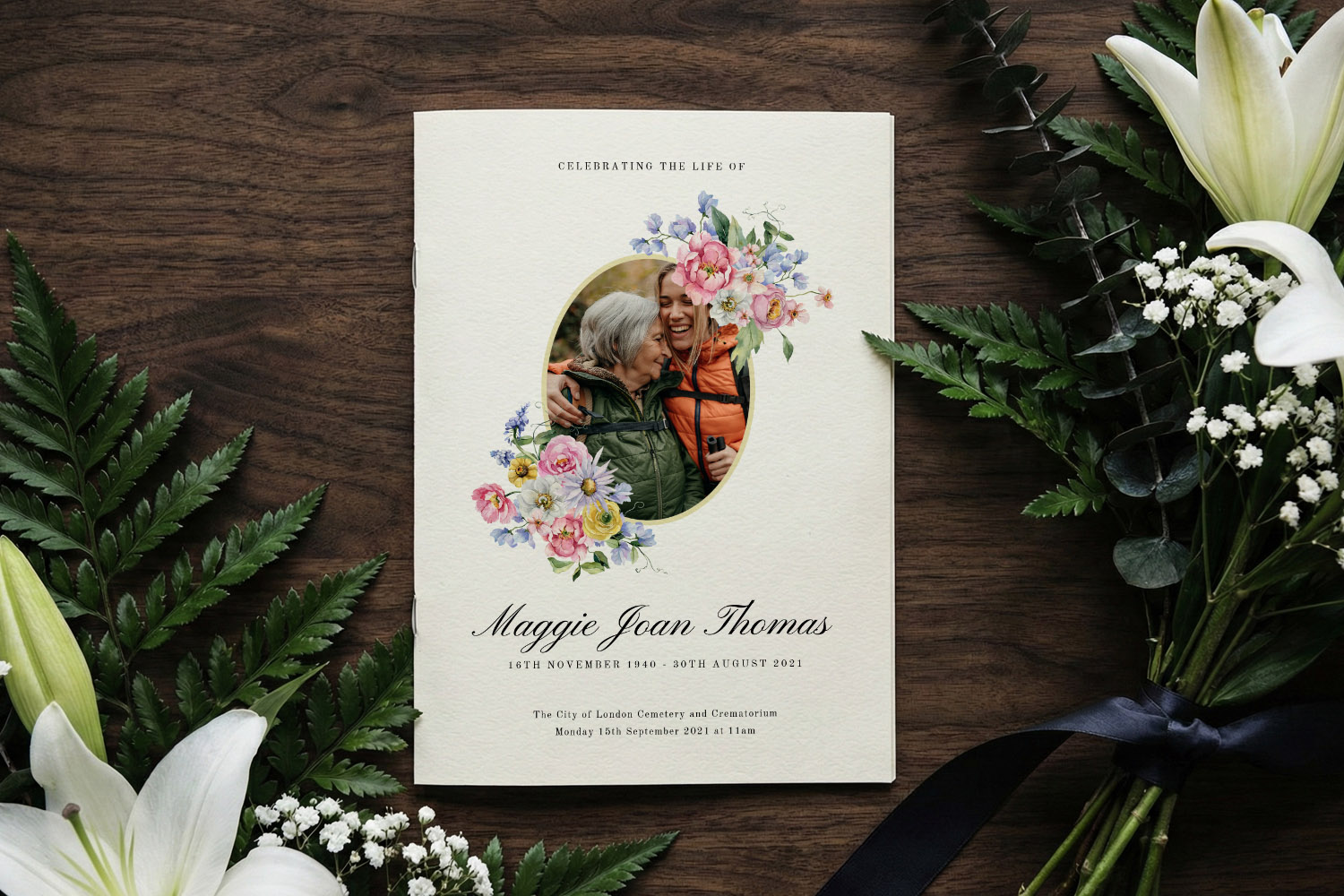 Funeral order of service booklet with floral design and personal photo, displayed on a wooden table with white lilies and