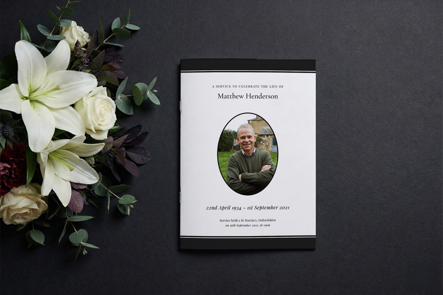 Funeral order of service booklet with a photo on the cover, white background, and elegant black border, beside white lilies.