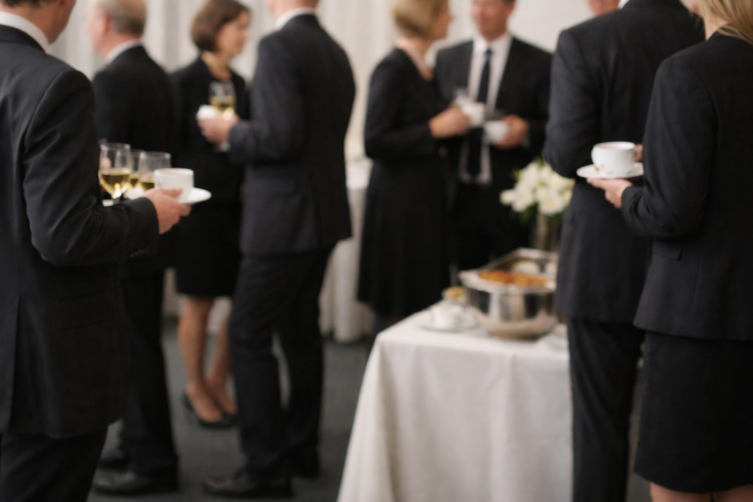 RSVP.studio funerals gathering with guests in formal black attire holding drinks near a refreshment table at a wake