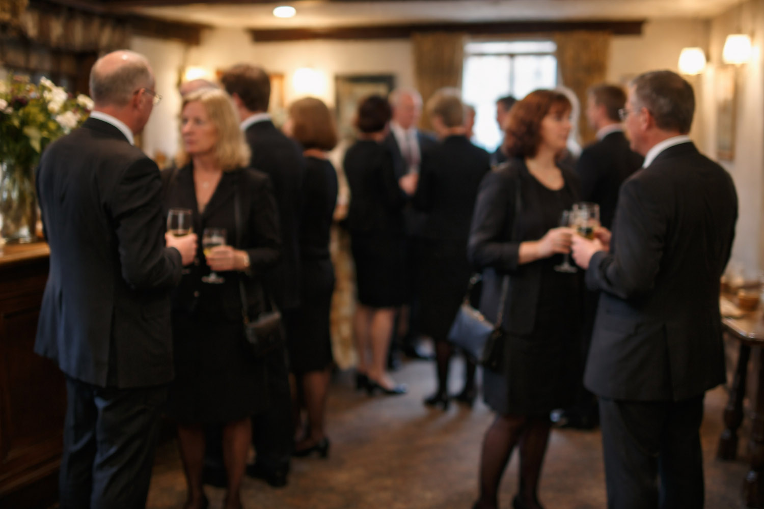 RSVP.studio funerals gathering with guests in formal black attire socialising and holding drinks in a softly lit venue