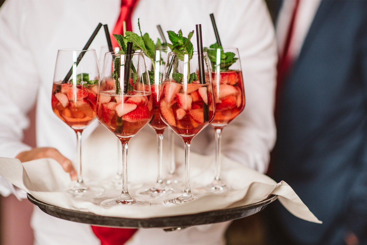 RSVP.studio event server holding a tray of fruit cocktails in wine glasses with ice, mint and straws, ready to be served