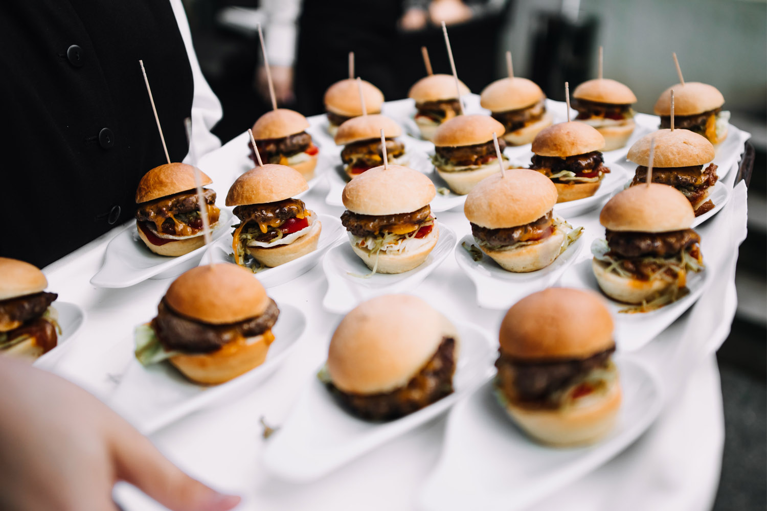 RSVP.studio event page catering with mini cheeseburgers served on individual plates, presented on a tray by staff.