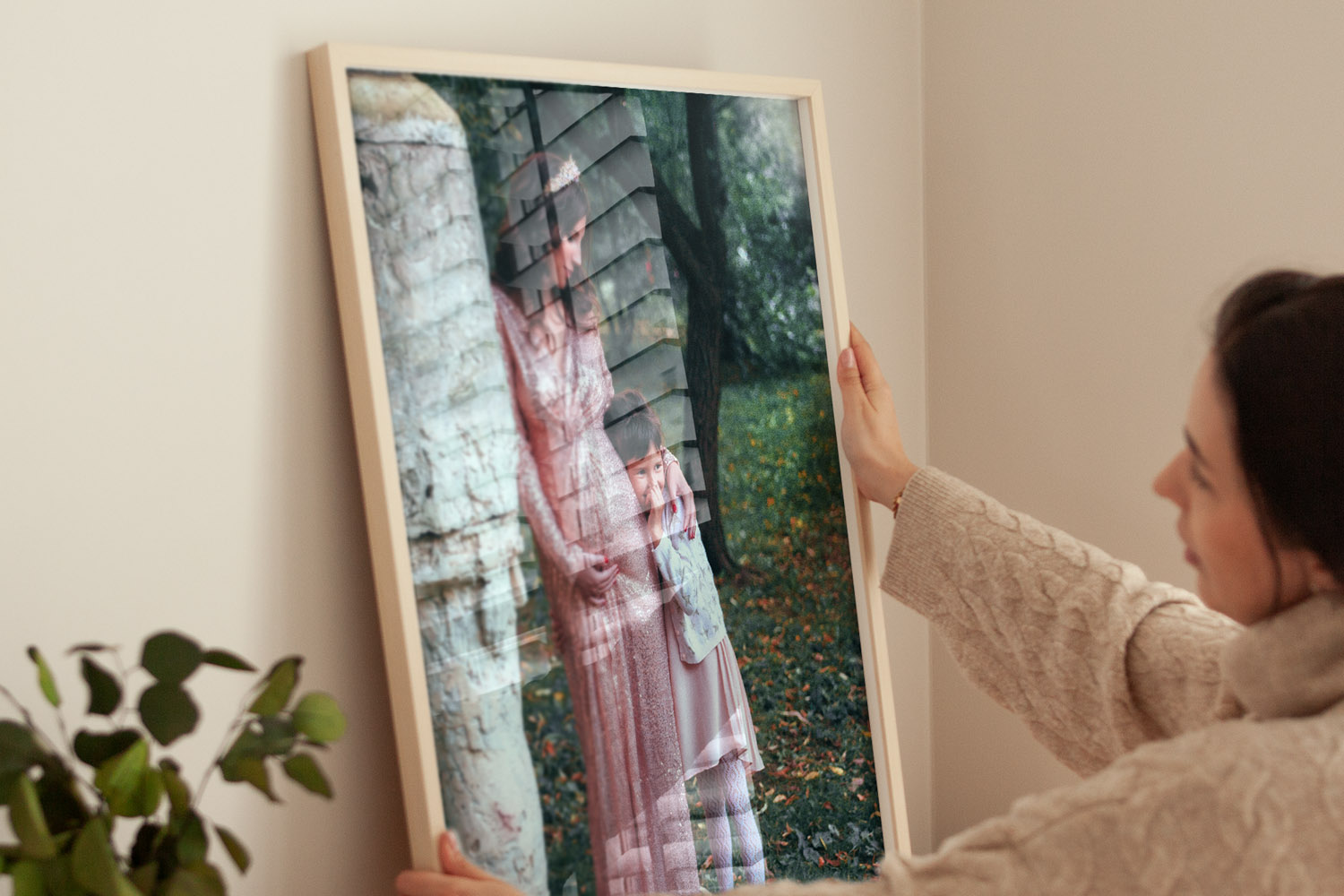 Simple framed prints with a light wood frame, held by a woman in a cosy room, featuring a reflective acrylic glazing.