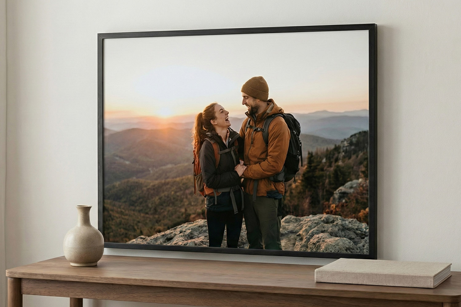 Simple framed prints featuring a couple hiking at sunset, displayed on a wooden console table against a white wall.