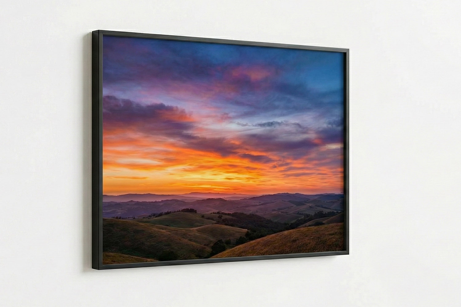 Simple framed prints featuring a vivid landscape sunset with rolling hills, displayed in a slim black frame on a white wall.