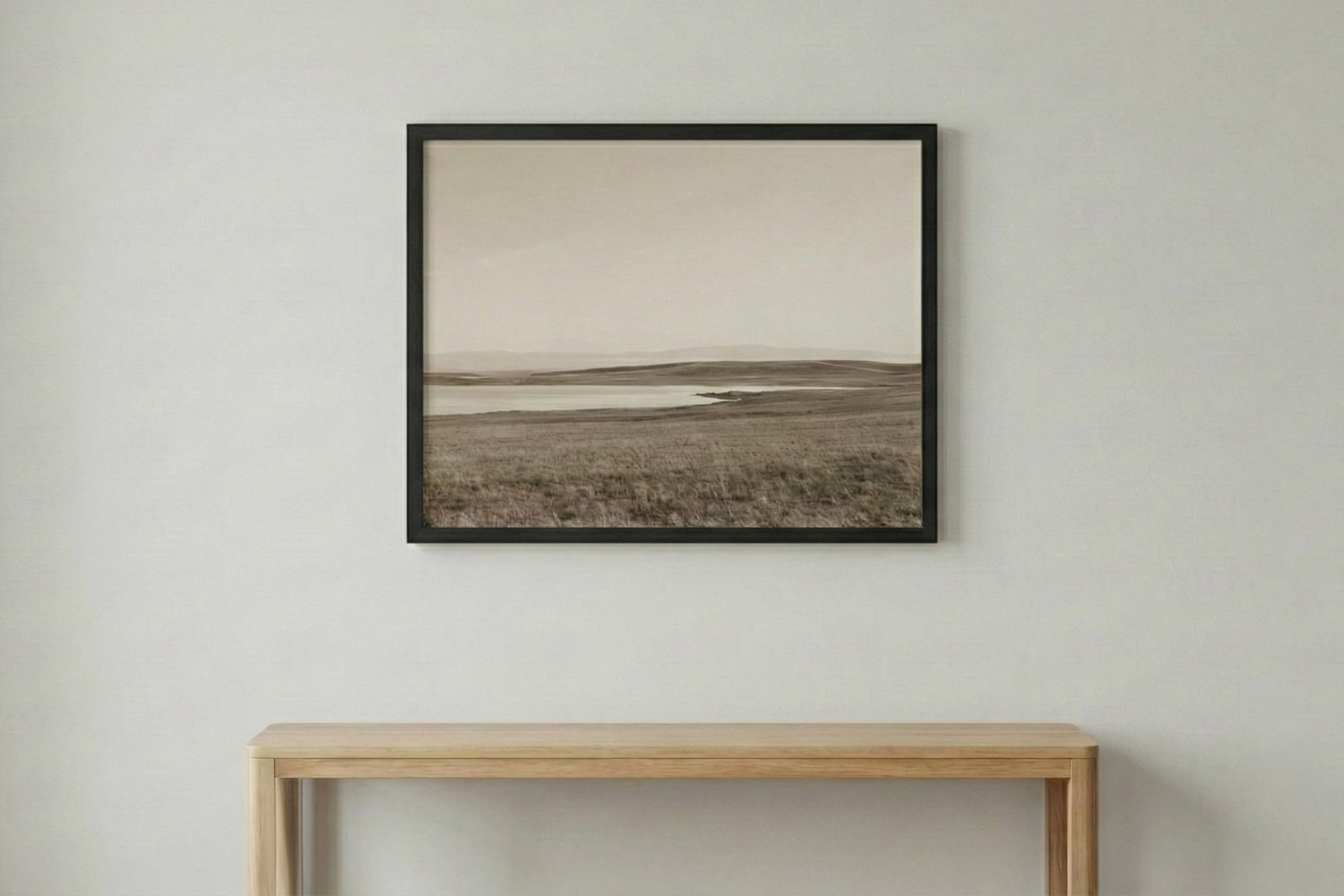 Simple framed prints featuring a black frame and sepia landscape artwork, hung above a light wood console table on a plain