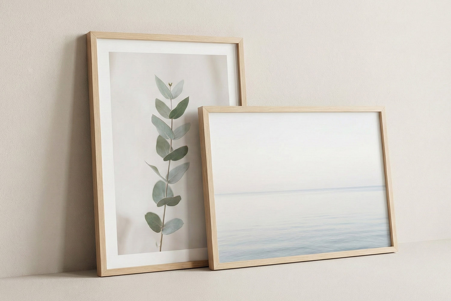 Simple framed prints with light wood frames, featuring minimalist botanical and seascape art, displayed against a neutral