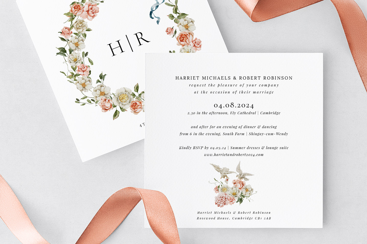 Wedding invitations with elegant floral wreath design and RSVP details, displayed with a peach satin ribbon on a light