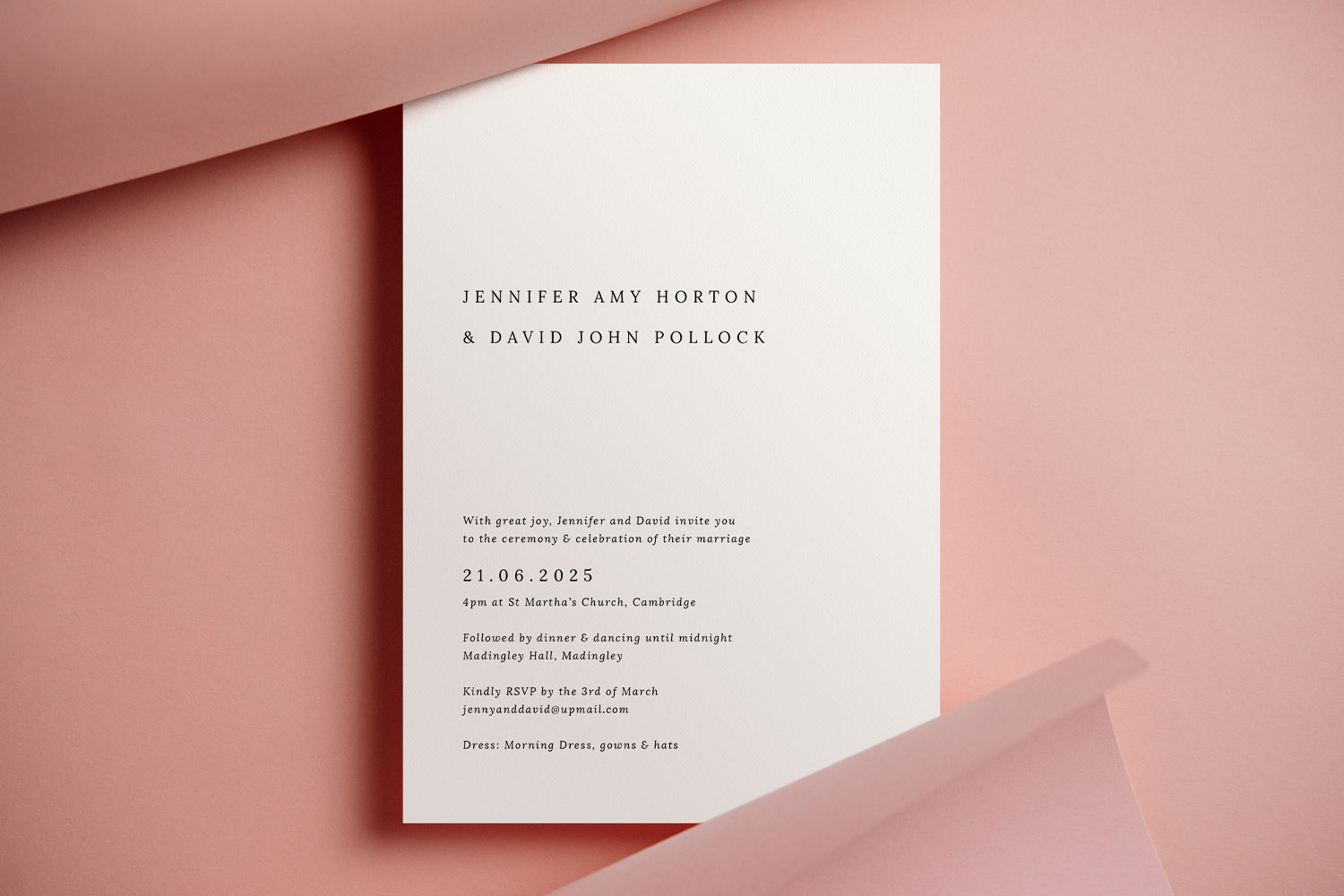 Wedding invitations with minimalist black text on white card, displayed on a soft pink background in a flat-lay arrangement.