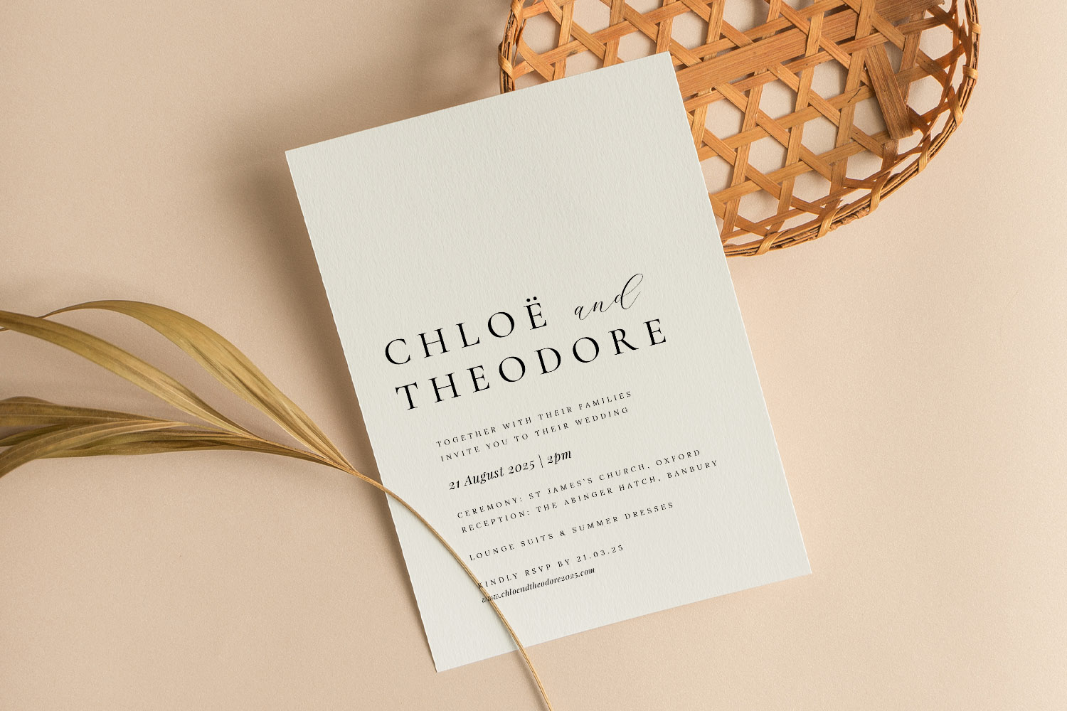 Wedding invitations with elegant black typography on textured white card, styled with dried foliage and a woven basket