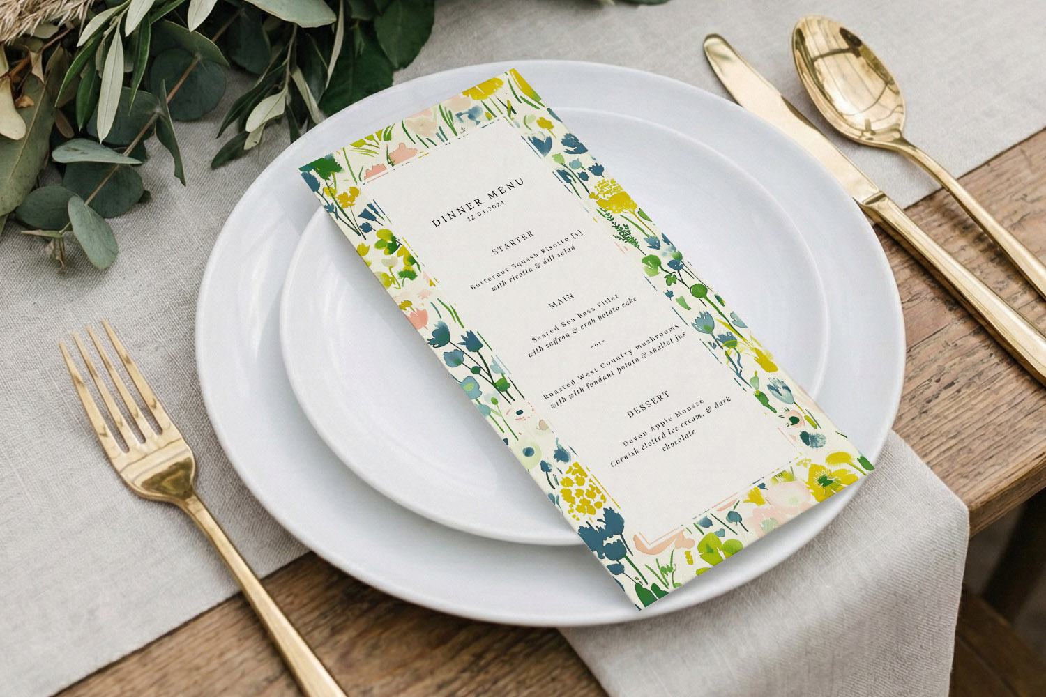 Wedding menus with a colourful floral border placed on a white plate, styled with gold cutlery and a linen tablecloth.