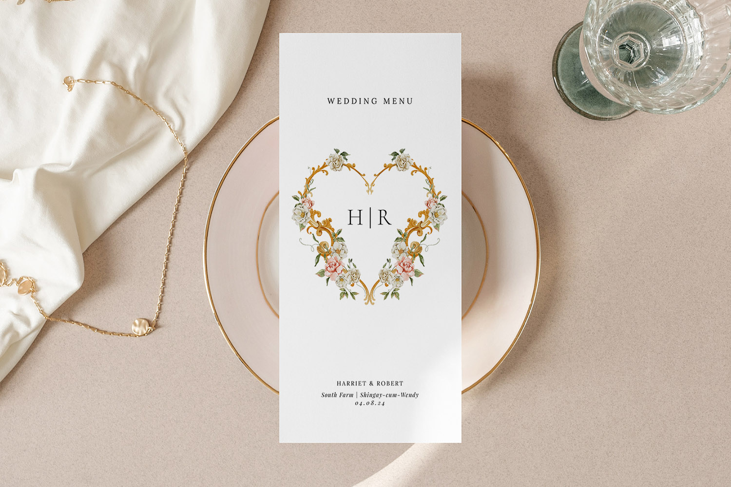 Wedding menu with elegant floral heart design, displayed on a white plate with gold trim and glassware on a beige table.