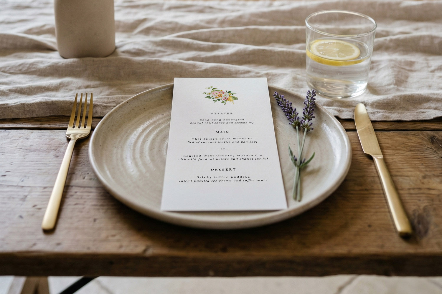 Wedding menus featuring a floral design card placed on a ceramic plate with lavender, gold cutlery, and a linen tablecloth