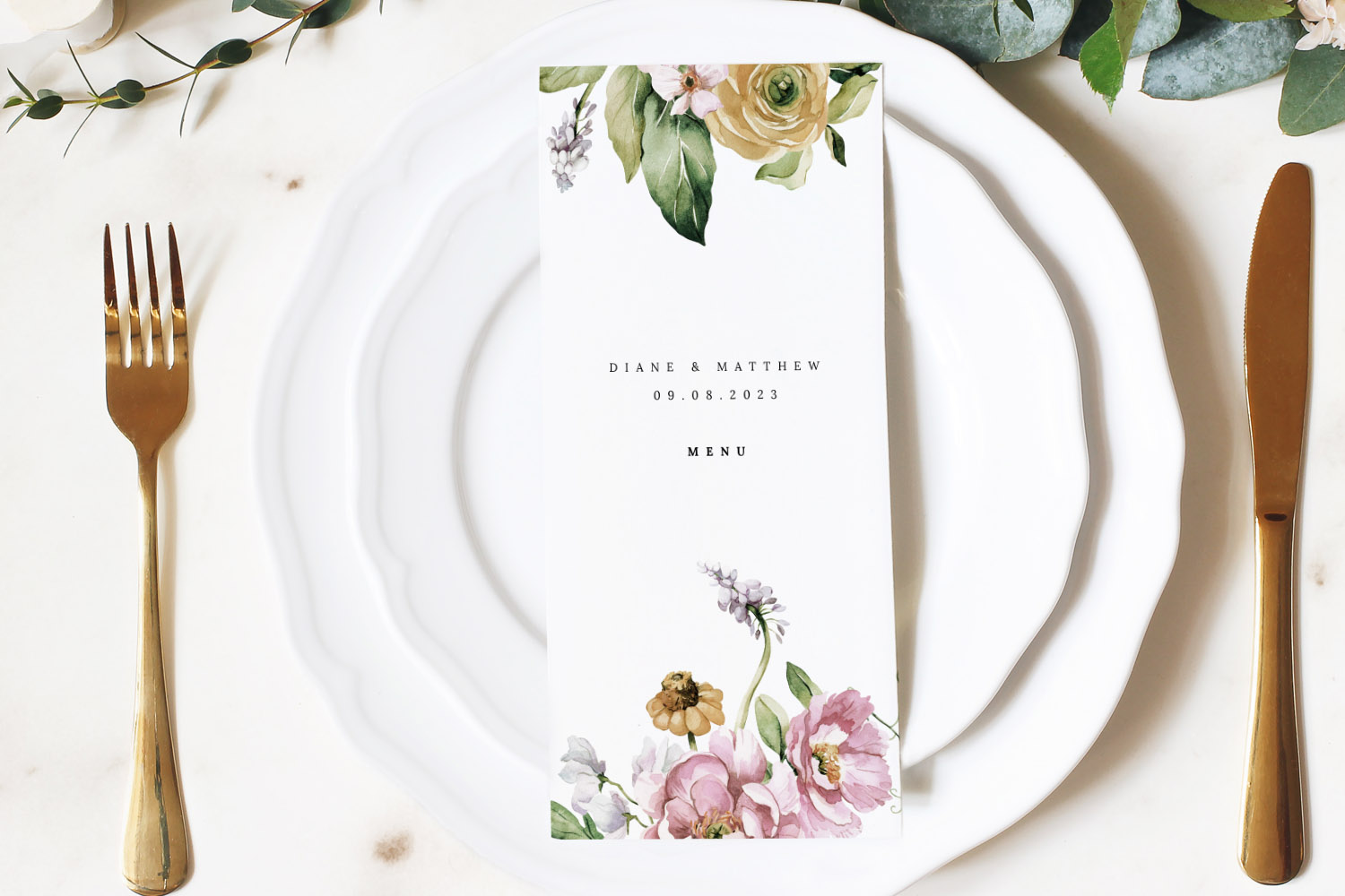 Wedding menus with floral design and elegant typography placed on white plates with gold cutlery on a marble table.