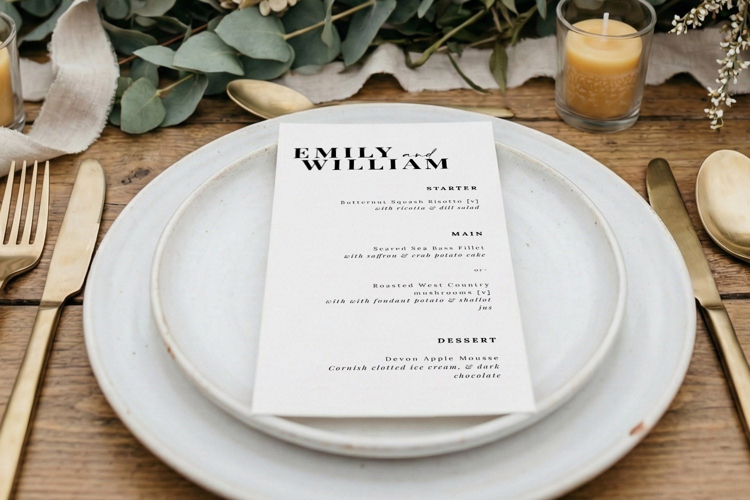 Wedding menus featuring a minimalist white design placed on a rustic table setting with gold cutlery and greenery accents.