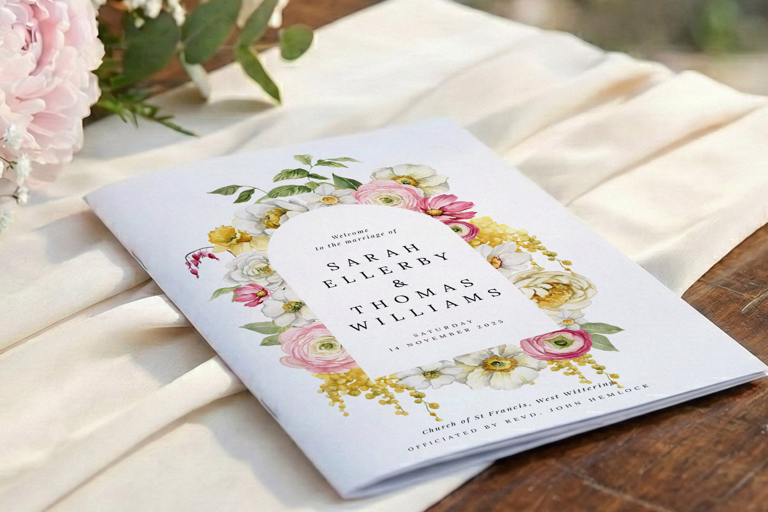 Wedding order of service booklet with floral cover design, personalised names and date, displayed on a cream fabric and