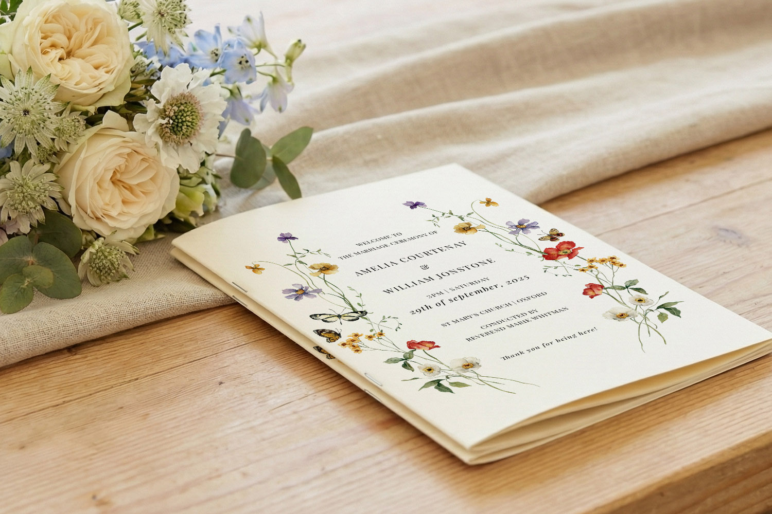 Wedding order of service booklet with floral cover design, displayed on a wooden table beside a bouquet of cream roses.
