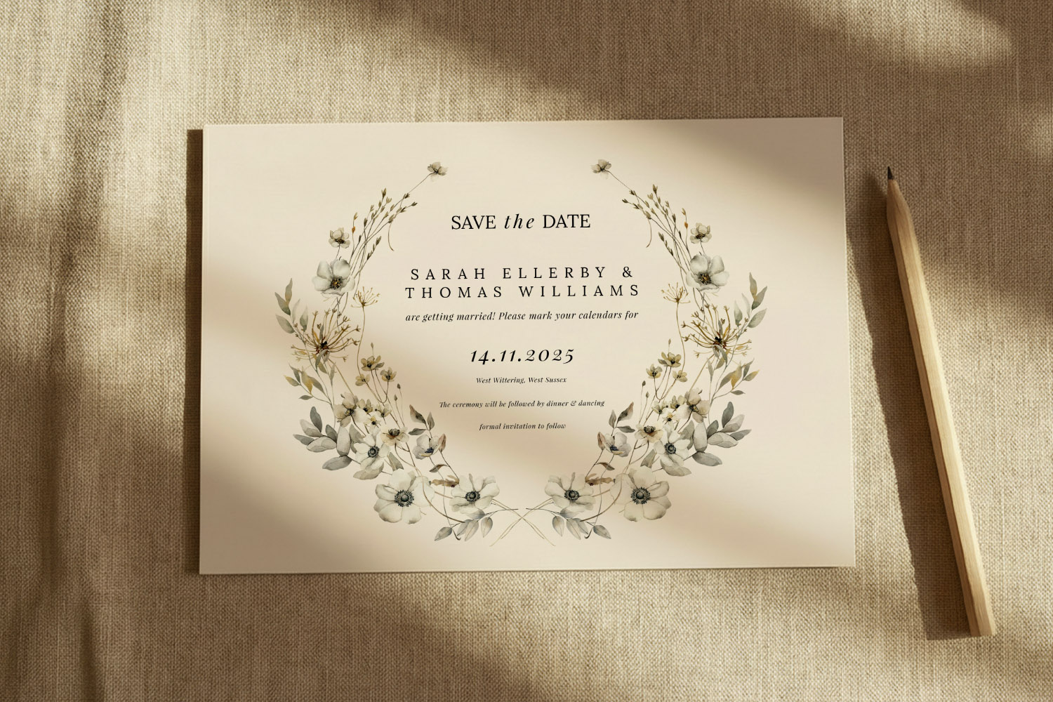 Wedding save the dates card with elegant floral wreath design, neutral tones, and modern typography on textured fabric