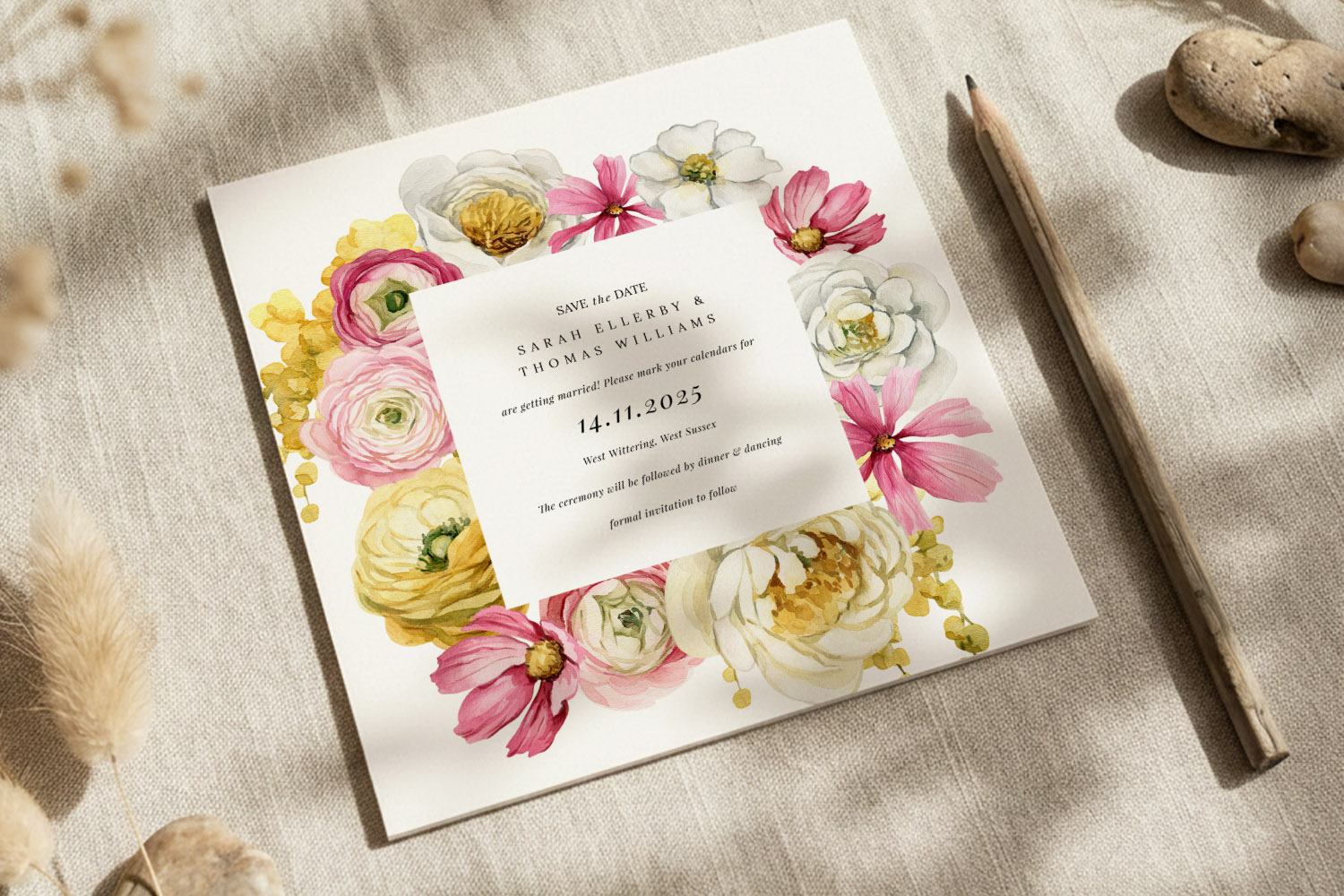 Wedding save the dates card with pink, yellow and white floral border, displayed on linen fabric with a pencil beside it