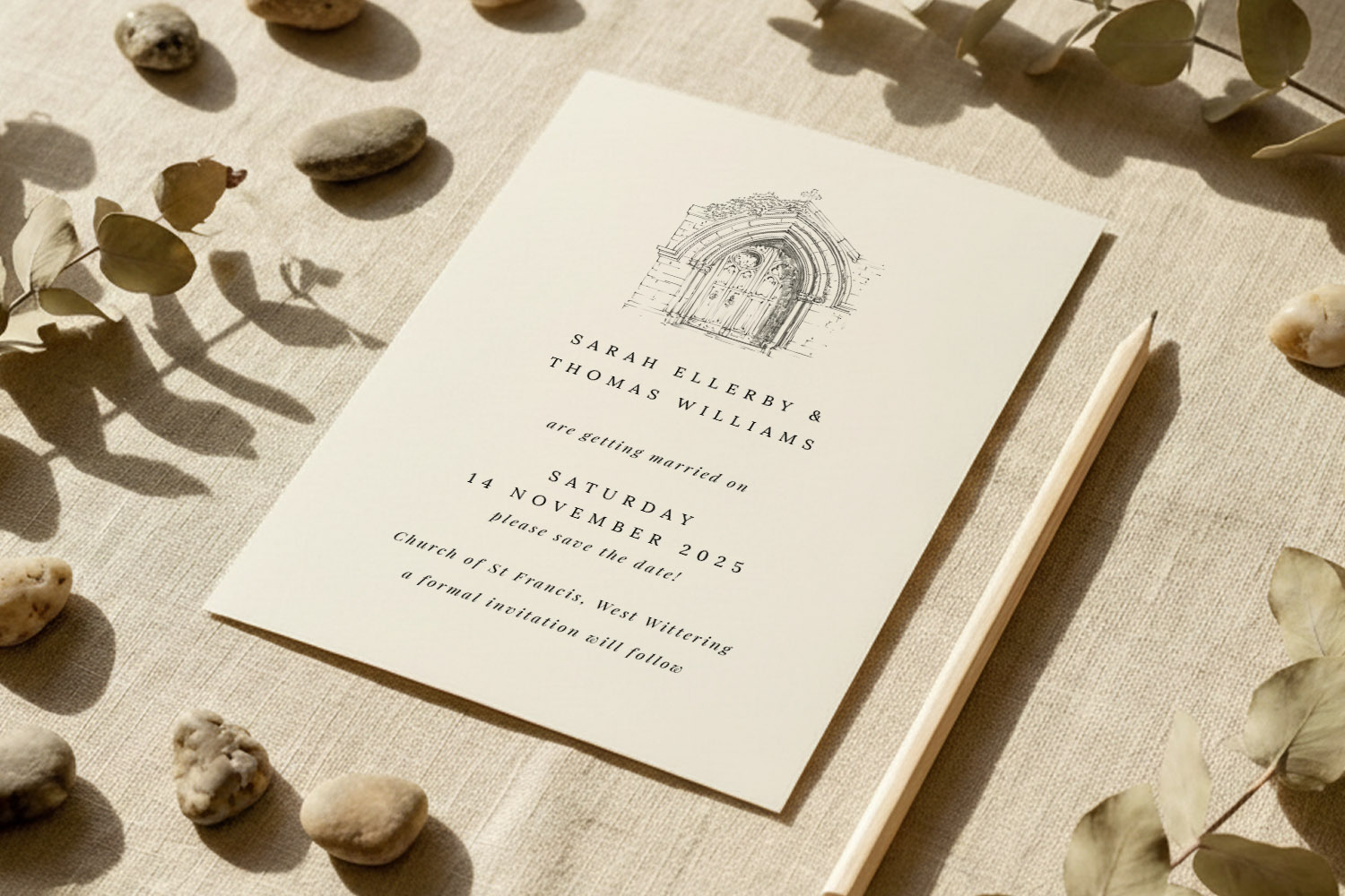 Wedding save the dates card with elegant black text and church illustration, styled on a linen cloth with pebbles and dried